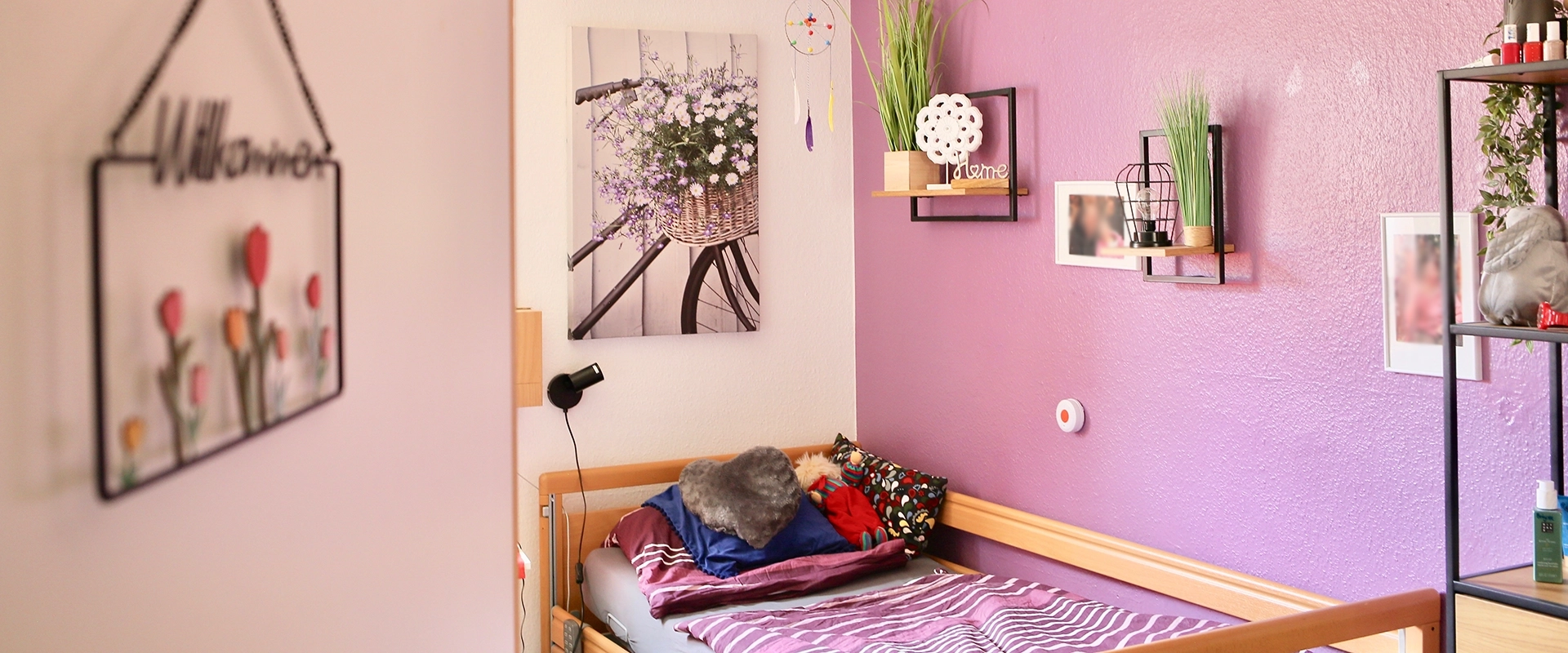 Blick in ein gemütliches Zimmer im betreuten Wohnen mit einer rosa Wand und einem bett mit Kuscheltieren.